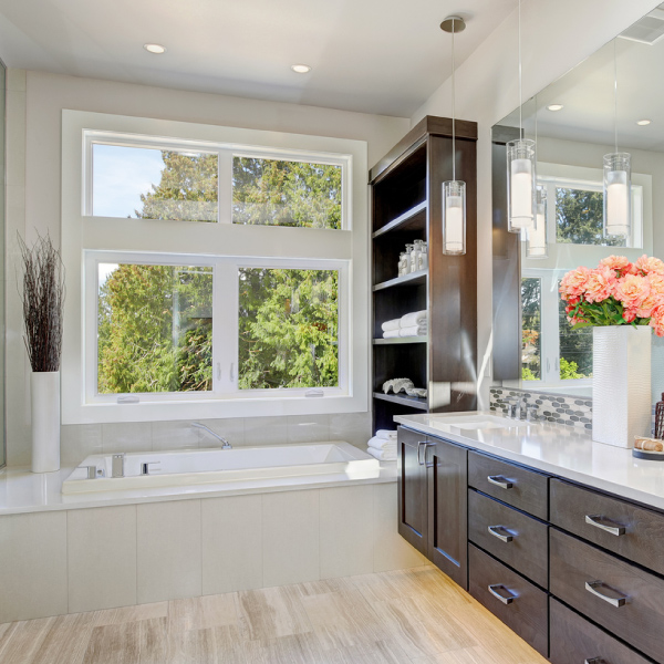 View of modern bathroom featuring bathtub below large window, cabinets, sink, and large sheet mirror.