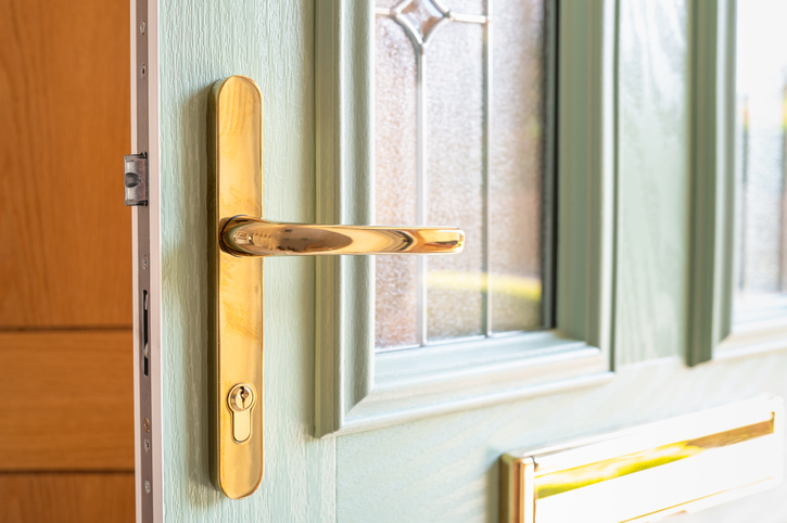 Brass door handle on pale green door with windows.